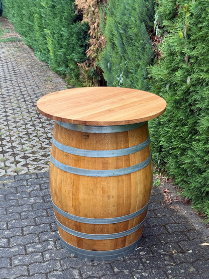 Weinfass-Stehtisch mit runder Wild-Eichenplatte und Metallringen auf gepflastertem Boden vor einer Hecke